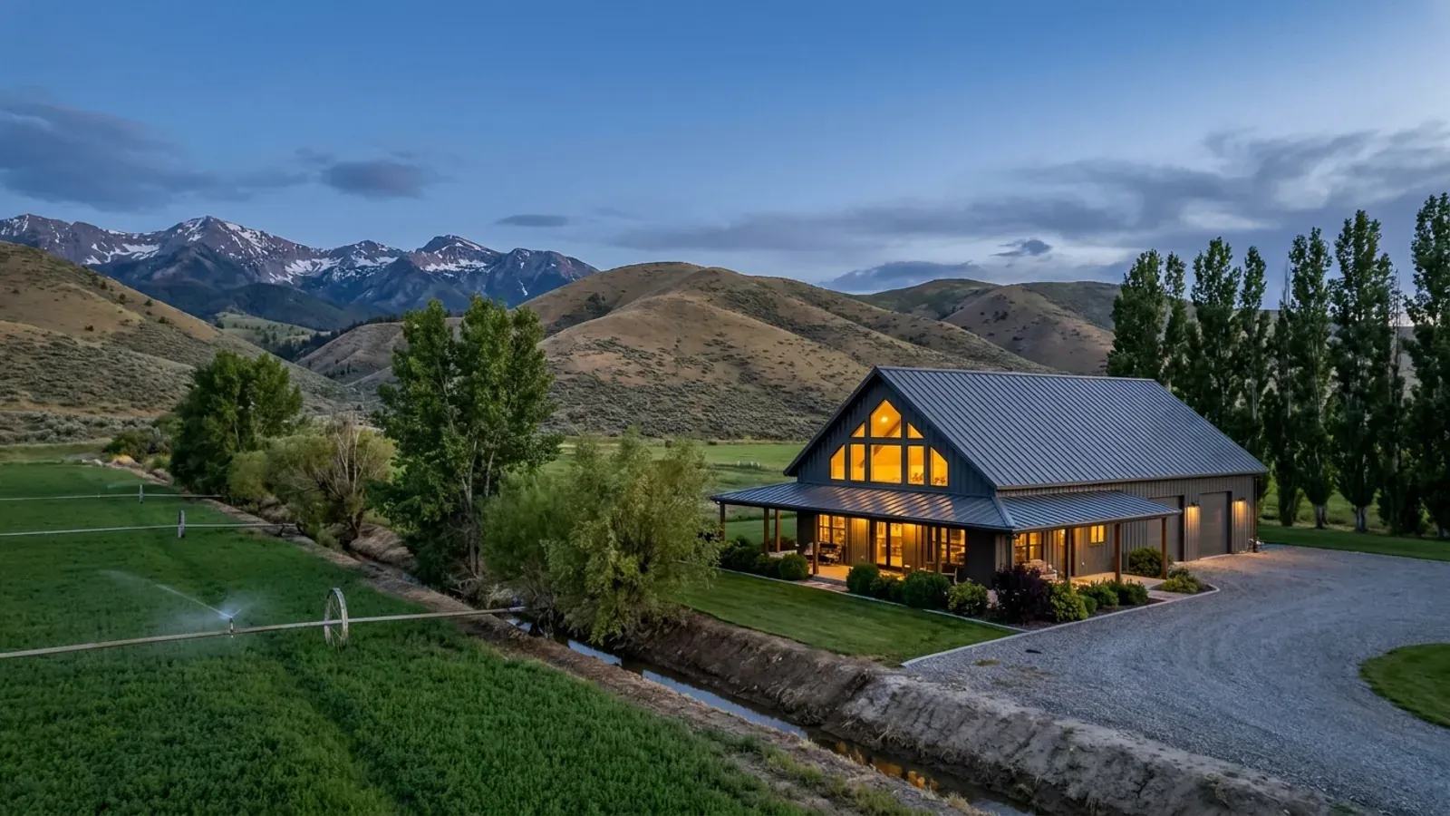A finished barndominium at dusk with warm interior lighting glowing through its large windows.
