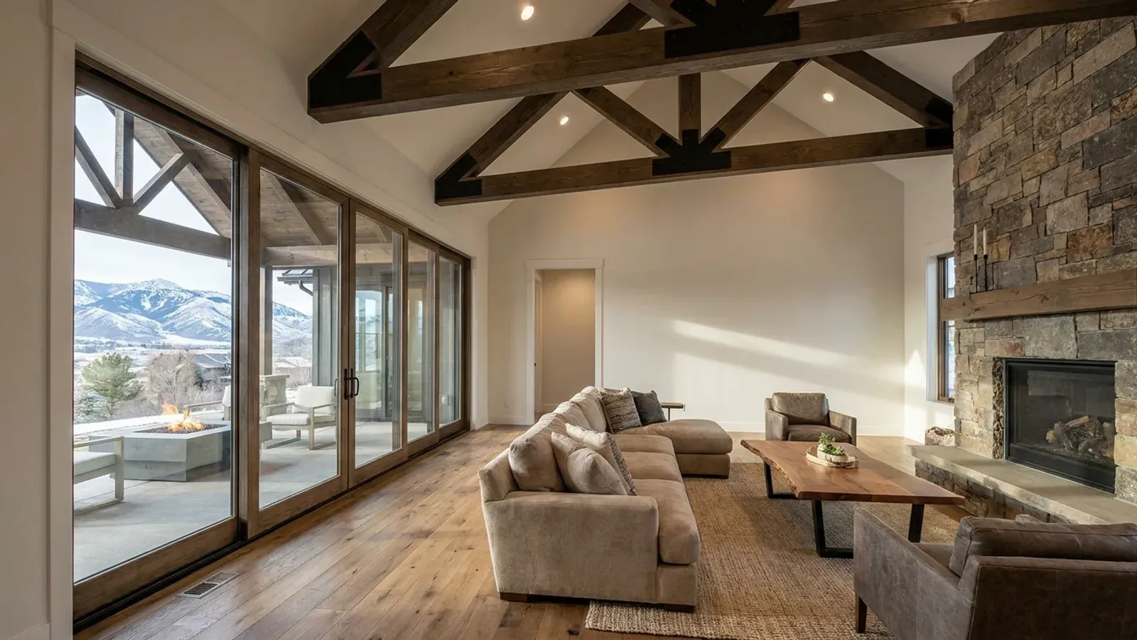A vaulted barndominium great room with exposed wood trusses, a wall of glazed sliding doors, and a stone-clad fireplace.