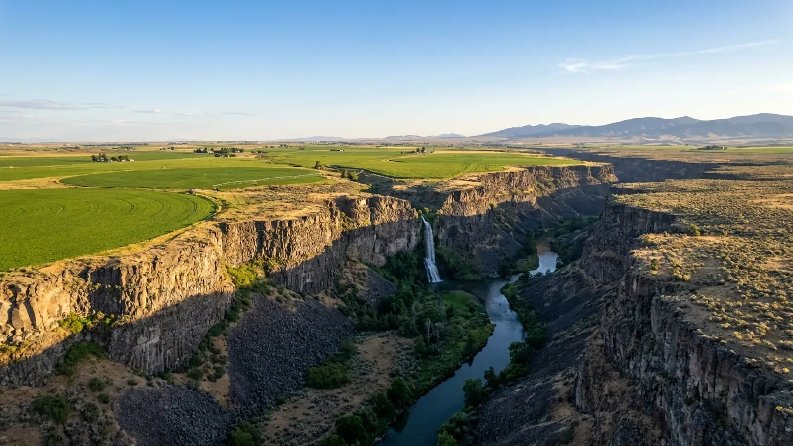The Snake River in a sheer basalt canyon below the flat Magic Valley rim, with green center-pivot fields stopping at the canyon edge.